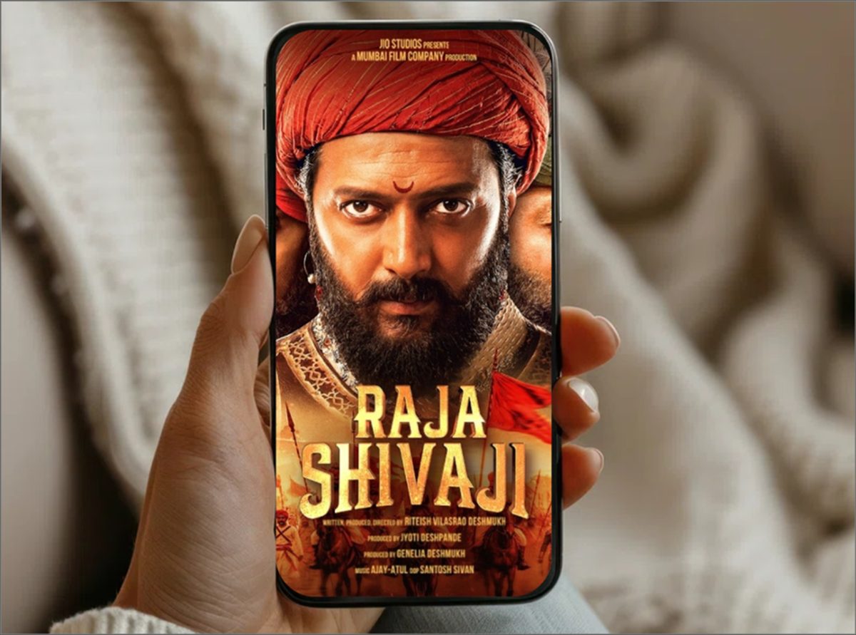 A phone held up showing a film's trailer poster, Raja Shivaji, ready to play
